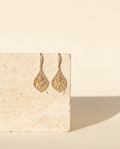 Uwairjan Drops — 18k gold openwork drop earrings on cream travertine