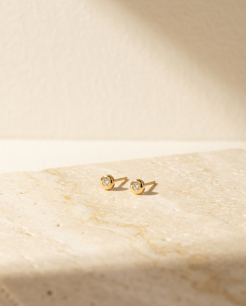 Aal Studs — 18k gold diamond stud earrings on cream travertine